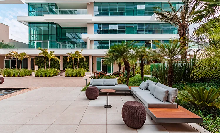 Terraço com jardim, sofás e palmeiras diante de fachada envidraçada, no Almaa Cabral