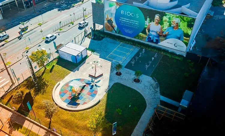 Vista aérea de praça com painel BIOOS no tapume e canteiro colorido