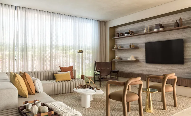 Sala de estar com sofá, poltronas, cortinas e televisão na parede de pedra