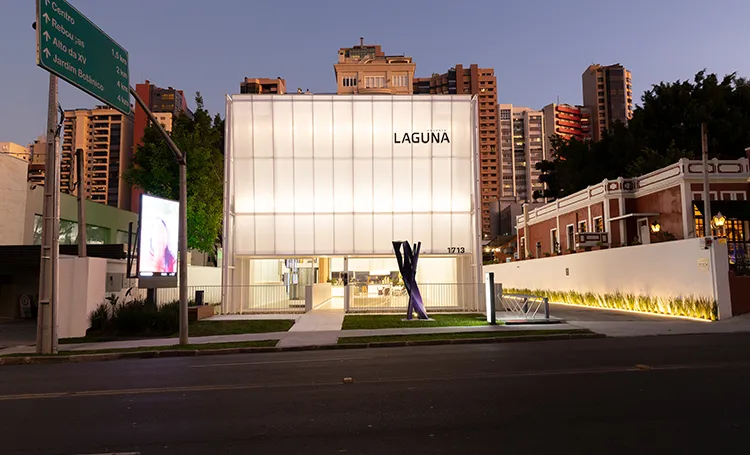 Fachada da Galeria Laguna ao anoitecer com prédios de Curitiba ao fundo