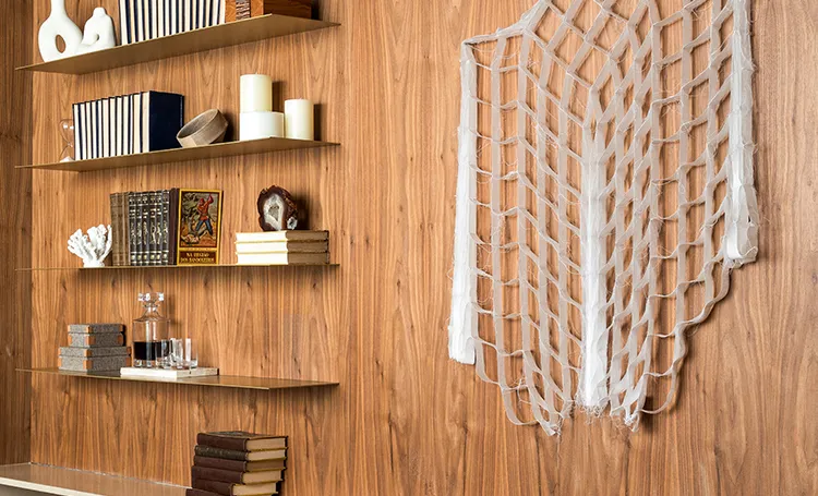 Estante de madeira com livros e objetos ao lado de peça de macramê