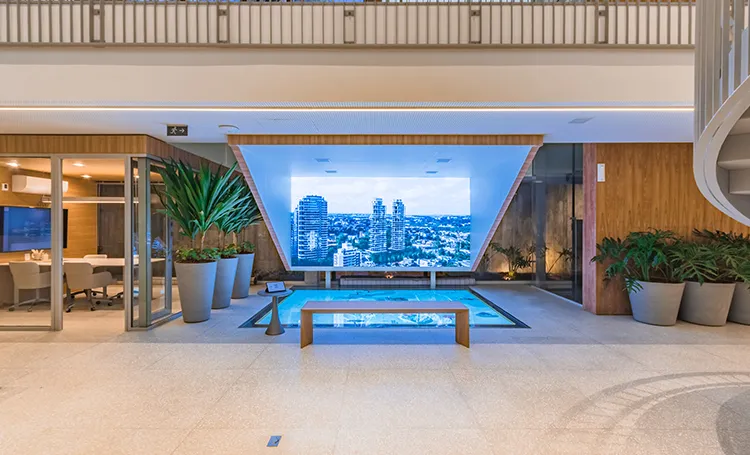 Salão da Galeria Laguna com piscina rasa, plantas e telão com vista da cidade