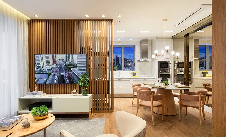 Sala com divisória ripada, TV e cozinha ao fundo