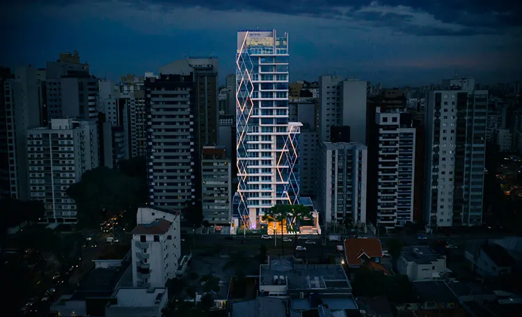 Torre do Llum Batel iluminada à noite entre prédios de Curitiba