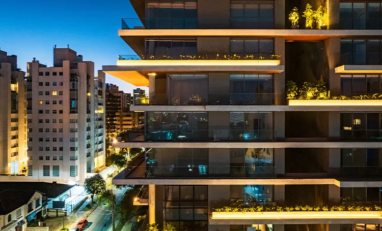 Fachada do PINAH ao anoitecer com varandas iluminadas e prédios ao redor