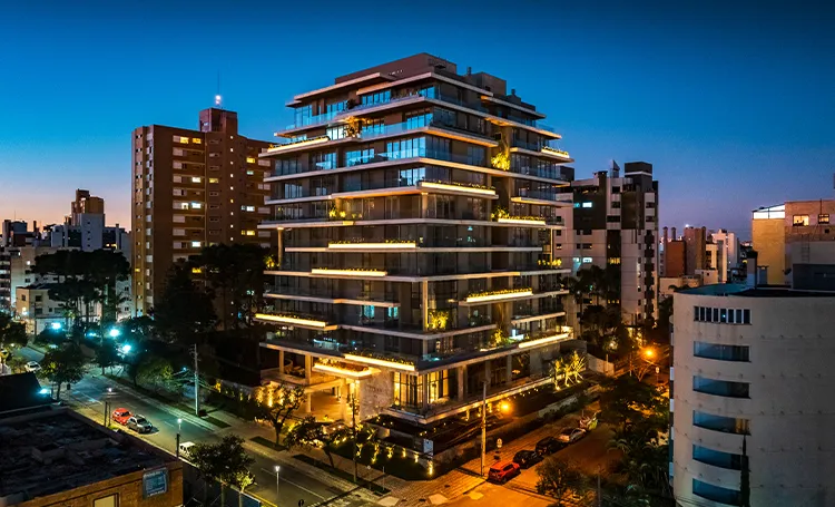Fachada do PINAH iluminada ao anoitecer, entre prédios de Curitiba
