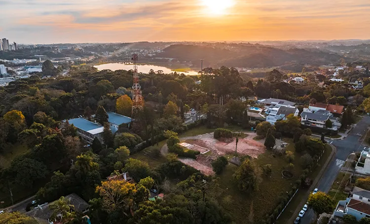 Pôr do sol sobre bairros arborizados e lago de Curitiba