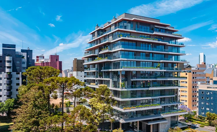 Edifício com varandas de vidro em meio a araucárias, em Curitiba