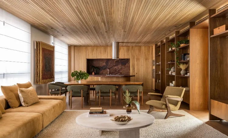 Sala de estar com sofá, mesa e estantes de madeira, em render do ZAHI Taunay