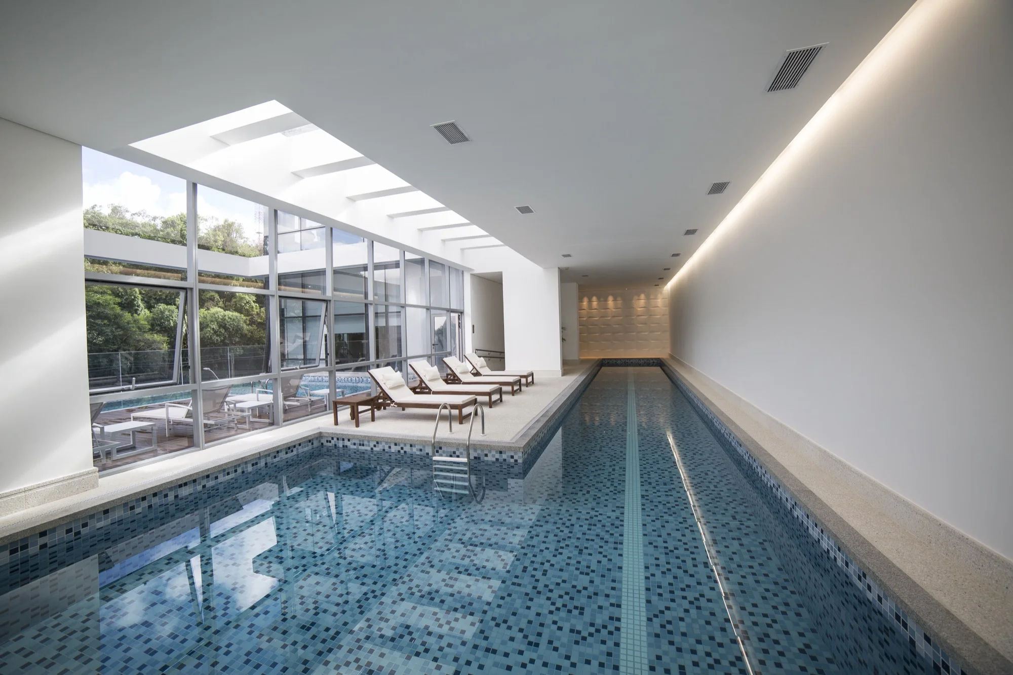 Piscina coberta com mosaico e espreguiçadeiras no EOS Barigui