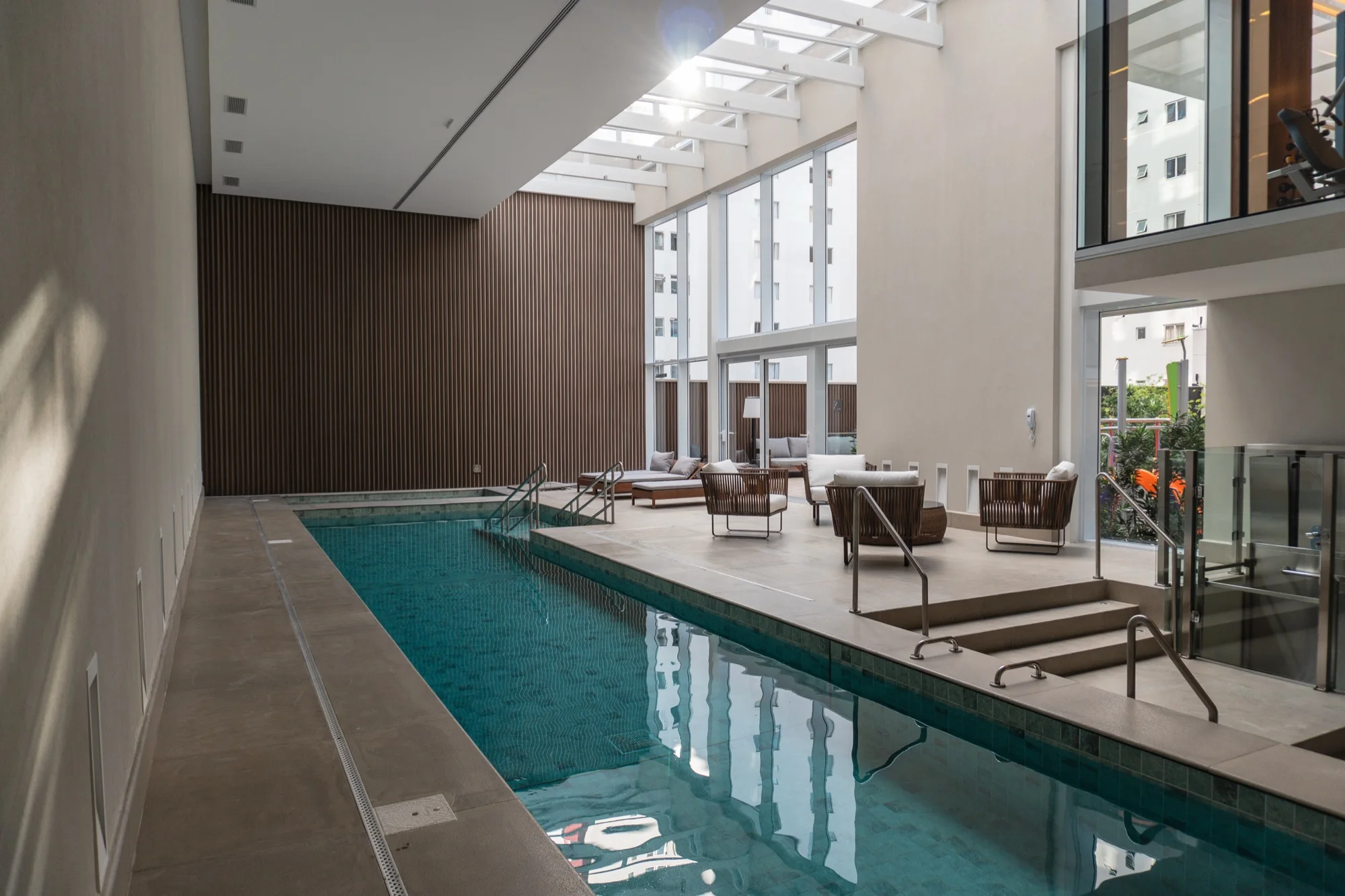 Piscina interna com deck e poltronas, LLUM Batel